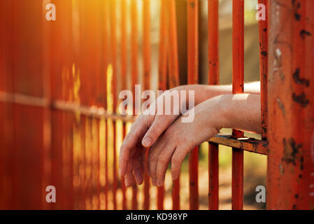 Female hands behind prison yard bars, incarcerated captivated person in jail Stock Photo