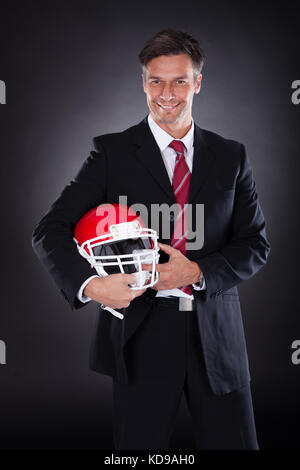 Mature Businessman Holding Red Rugby Helmet Over Black Background Stock Photo