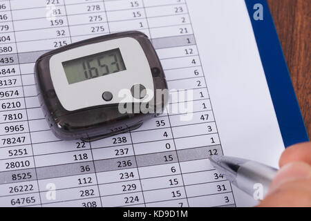 Close-up Of Hand Holding Pen Over Sheet With Digital Pedometer Stock Photo