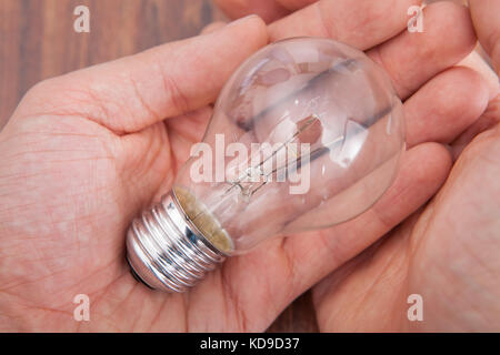 Close-up Of Person's Hand On Wooden Table Holding Bulb Stock Photo