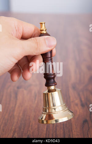 Close-up Of Person Hand On Wooden Table Holding Bell Stock Photo
