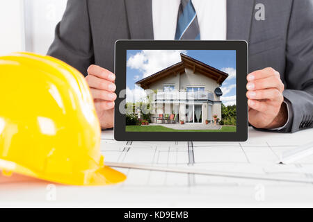 Close-up Of Male Architect Holding Digital Tablet In Front Of Hardhat Stock Photo
