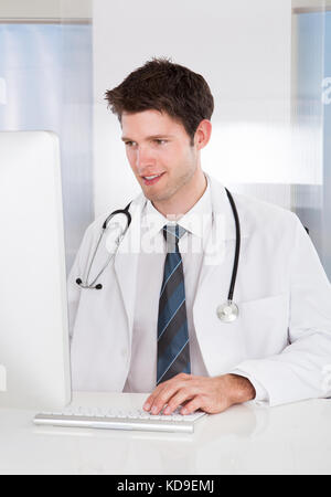 Portrait Of Happy Male Doctor Using Computer At Desk In Clinic Stock Photo