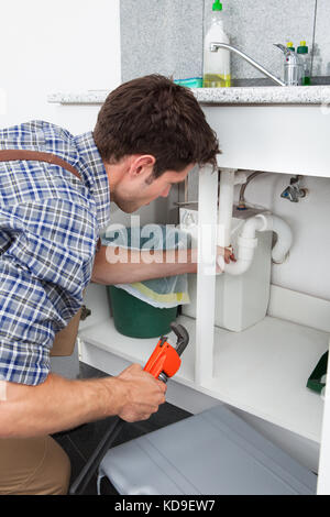 Young Plumber Working With Pipe Wrench In Kitchen Stock Photo