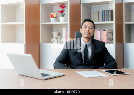 Young business man with fake eyes painted on paper stickers sleeping at  workplace in office Stock Photo