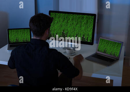 Young Man Sitting At Desk Using Laptop And Computer At Home Stock Photo