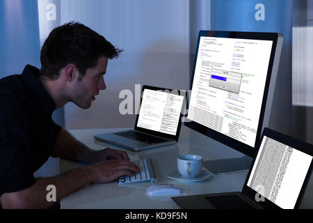Young Man Sitting At Desk Working On Computer And Laptop At Home Stock Photo