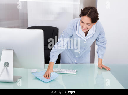 Portrait Of Happy Female Janitor Cleaning Desk At Office Stock Photo