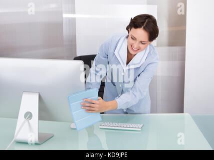 Portrait Of Happy Female Janitor Cleaning Desk At Office Stock Photo