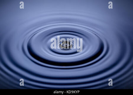 Droplet splash on water surface making circles Stock Photo