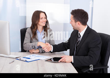 Businesswoman Looking At Businessman While Shaking Hand At Office Desk Stock Photo