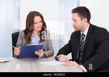 Man Looking At Businessman Writing On Clipboard Stock Photo