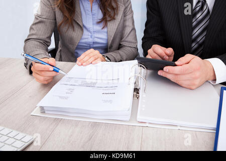 Two Young Businesspeople Calculating Bills At Desk In Office Stock Photo