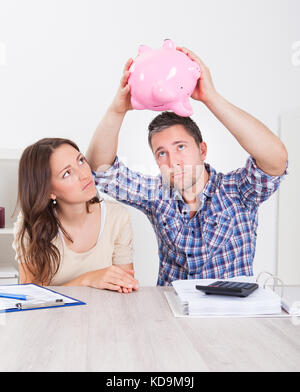 Woman Looking At Piggybank Raised By Young Man Stock Photo