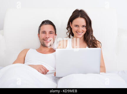 Portrait Of Smiling Couple Lying On Bed Using Laptop Stock Photo