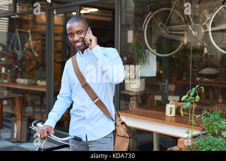 Smiling man standing with a bike talking on a cellphone Stock Photo
