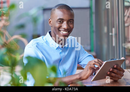 Smiling young African man working online at a sidewalk cafe Stock Photo