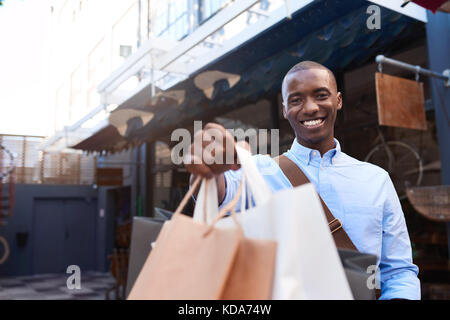 Smiling young man standing outside holding up shopping bags Stock Photo