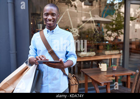 Smiling young man using a digital tablet while out shopping Stock Photo