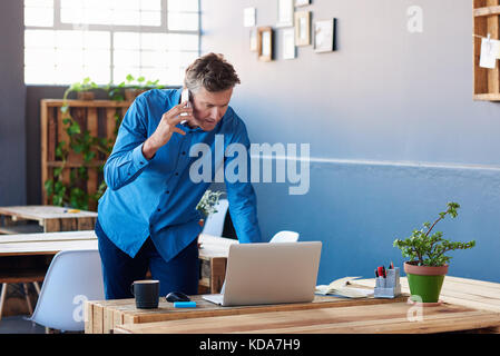 Focused businessman talking on his cellphone and using a laptop Stock Photo