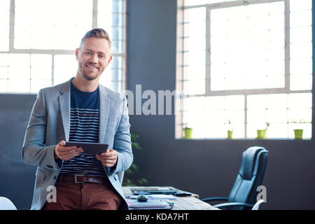 Smiling young businessman using a tablet in an office Stock Photo