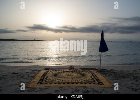 A scenic view of La Pelosa beach at sunrise in summer. A beach towel and umbrella in the sand with sea in background. Stock Photo