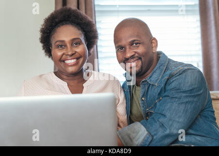 Smiling African couple sitting at home together using a laptop Stock Photo