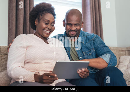 Smiling African couple sitting at home using a digital tablet Stock Photo