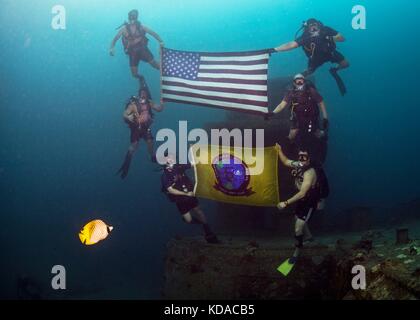 U.S. Navy sailors hold up the American flag and their units flag while scuba diving at the American Tanker wreck near Naval Base Guam June 21, 2017 in Apra Harbor, Guam. The American Tanker is a sunken concrete barge that was used to transport fuel during World War II. Stock Photo