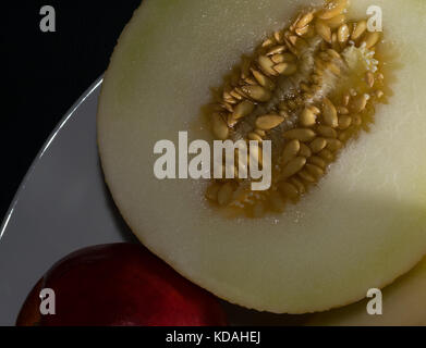 White melon cantaloupe with a red peach on a white plate. Dark background. Close up Stock Photo