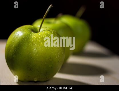 Three apples arranged in a diagonal line on a wooden surface with dark background Stock Photo