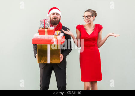 Its so hard and i tired! Not my problem, everything fine. Bearded man holding many gift box and crying, women looking at camera, toothy smiling and ha Stock Photo