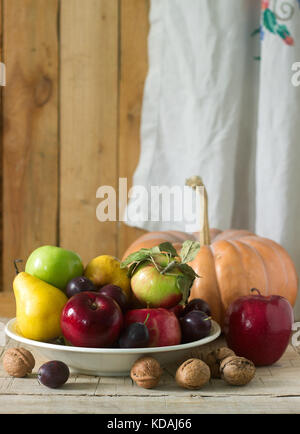 Autumn still life with apples, pears, plums, pumpkin and walnuts on a wooden background. Rustic style, selective focus. Stock Photo
