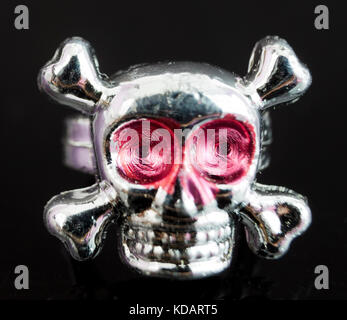 Close up of toy plastic silver skull and crossbones ring on black background. Stock Photo