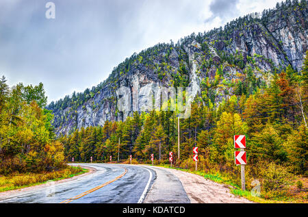 Highway road in stormy misty and foggy weather in mountain Charlevoix region of Quebec, Canada with turn during autumn with orange foliage Stock Photo