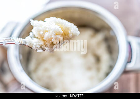 Macro closeup of spoonful of fresh cooked rice by cooking pot on table showing detail and texture Stock Photo