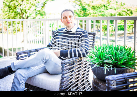 Young man sitting on chair outside on balcony in house or apartment Stock Photo