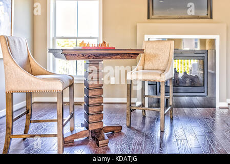 Closeup of chessboard table with wooden pieces in sunlight on loft of house with fireplace and chairs Stock Photo