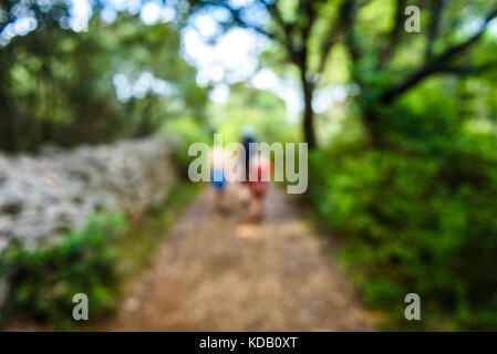 Family hiking on country road with rock fence and woods. Mother and daughters are trekking through rough terrain on island Silba Croatia. Intentionall Stock Photo