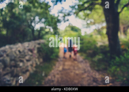 Family hiking on country road with rock fence and woods. Mother and daughters are trekking through rough terrain on island Silba Croatia. Intentionall Stock Photo