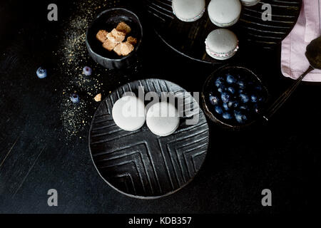 Dark monochrome photography. Grey cakes macaroons on the dark surface of the table, next to a spoon and sugar bowl with brown sugar.And pink towels of plain cloth Stock Photo