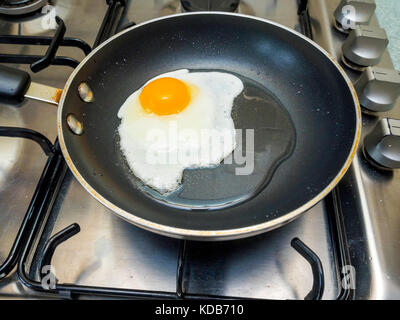 An egg being fried in sunflower oil in a small Teflon coated non stick frying pan on a gas hob Stock Photo