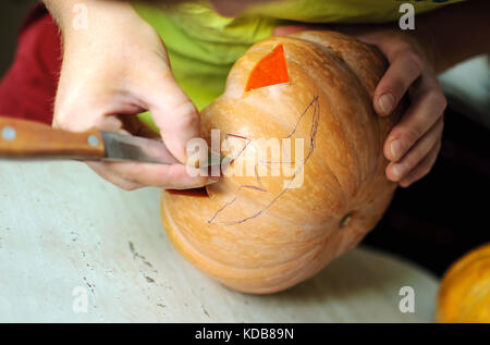 Halloween pumpkin cutting process, process of making Jack-o-lantern. Male hands with knife, leftovers of pumpkin on the kitchen table. Selective focus Stock Photo