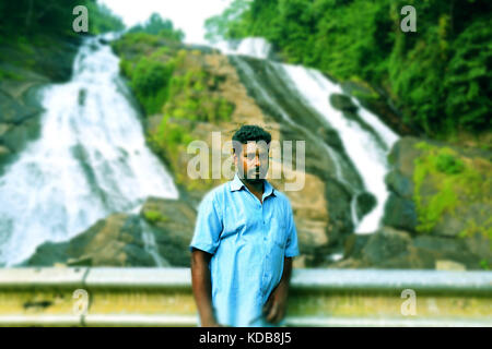 Young man smiling and standing in pose with big waterfall in the background. Stock Photo