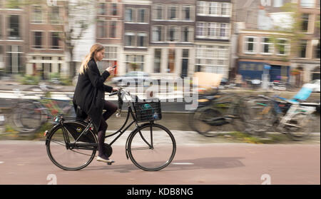 A young woman checks her phone as she cycles through Amsterdam Stock Photo
