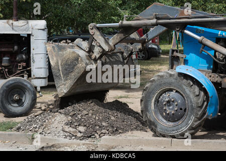Tractor pours out the old layer of asphalt on the roadside Stock Photo