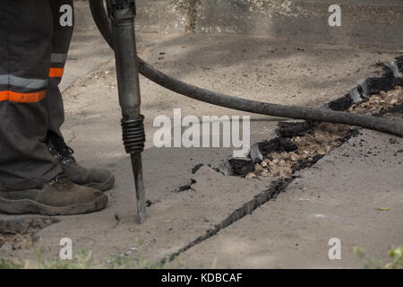 Road repairing works with jackhammer. Male worker using jackhammer pneumatic drill machinery on road repair. Stock Photo