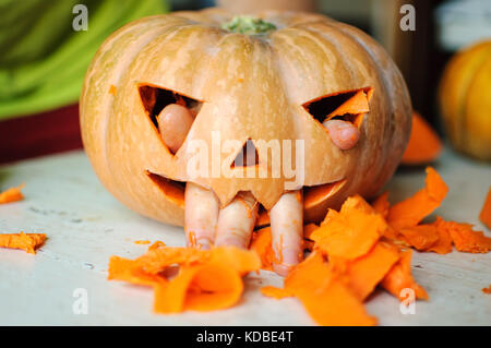 Process of making Jack-o-lantern. Funny picture of Halloween pumpkin monster face with male fingers. Selective focus and bokeh. Stock Photo