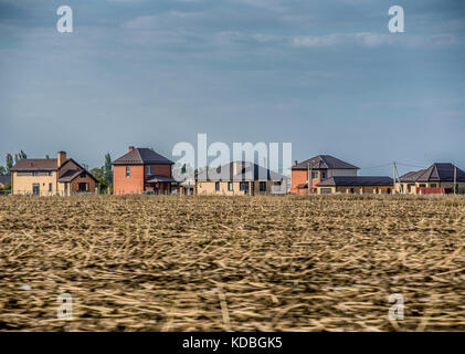 A view of the houses of a cottage village through an agricultural field. Autumn harvest is harvested from the field recently. Stock Photo