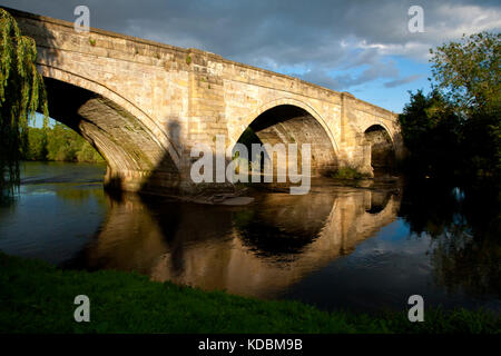 sun falling on stone bridge with a heavy grey clouds and blue sky behind Stock Photo